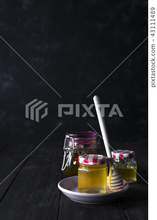 glass jar of honey and stick on a ceramic plate on a dark concrete background , copy space 43111489