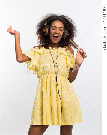 Young pretty african american woman in yellow dress singing and dancing with hair dryer instead Young pretty african american woman in yellow dress singing and dancing with hair dryer instead 43114975