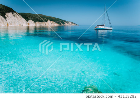 Lonely white sailing catamaran boat drift on calm sea surface. Pure shallow azure blue bay water of Lonely white sailing catamaran boat drift on calm sea surface. Pure shallow azure blue bay water of 43115282