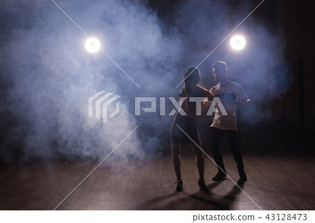 Skillful dancers performing in the dark room under the concert light and smoke. Sensual couple Skillful dancers performing in the dark room under the concert light and smoke. Sensual couple 43128473