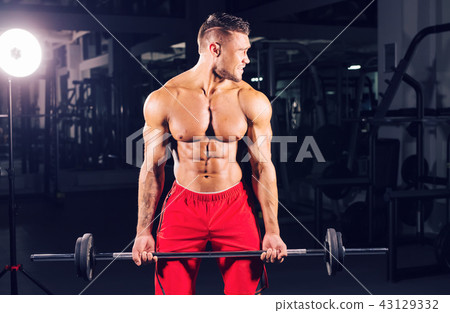 Bodybuilder doing the exercises with barbell. Strong male with naked torso on dark background Bodybuilder doing the exercises with barbell. Strong male with naked torso on dark background 43129332