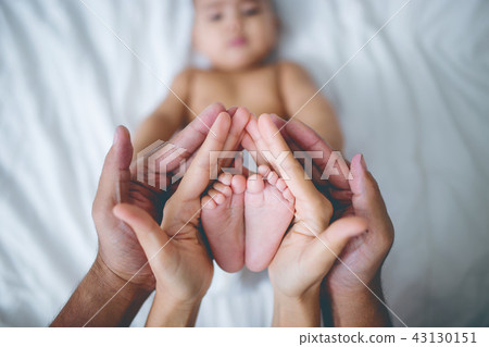 Hands of parents holds baby feet on the bed. 43130151