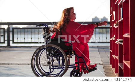Beautiful Red-Haired Girl In A Wheelchair Takes Out Of The Shelf Book 43141774