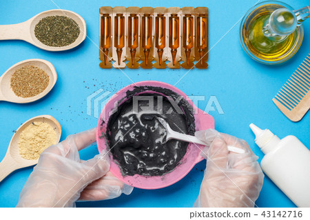 Photo from above with pink cup with black clay, mask oil, wooden spoons, comb, human hands with 43142716