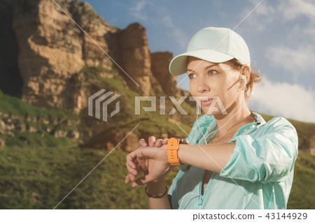 Portrait of a smiling young fitness girl in a cap and headphones checking her smart clock while Portrait of a smiling young fitness girl in a cap and headphones checking her smart clock while 43144929