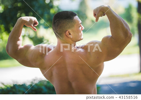 Man a strong inflated body shows off the muscles on his body in the park Man a strong inflated body shows off the muscles on his body in the park 43158516