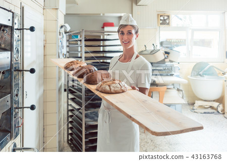 Baker woman presenting bread on board in bakery Baker woman presenting bread on board in bakery 43163768
