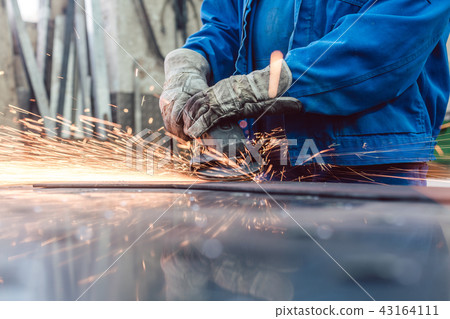 Worker in metal factory grinding workpiece with sparks flying 43164111
