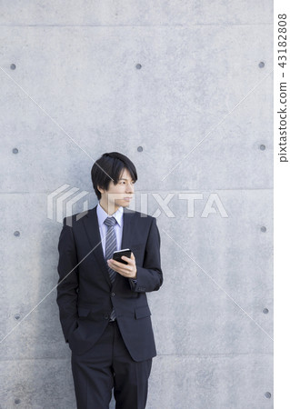 A businessman leaning against the wall with a smartphone 43182808
