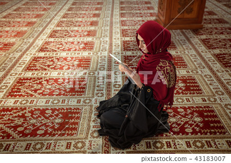 Young muslim woman praying in mosque with quran on tablet Young muslim woman praying in mosque with quran on tablet 43183007