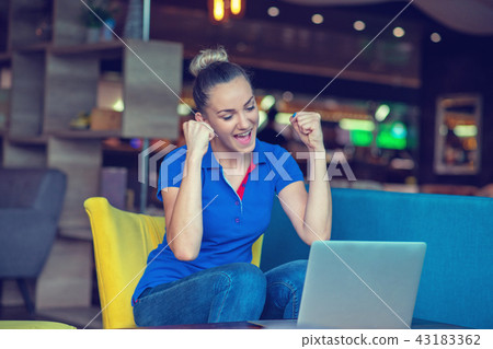 Winner girl euphoric watching a laptop in a coffee shop wearing a blue shirt 43183362