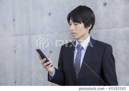 A businessman leaning against the wall with a smartphone 43183585