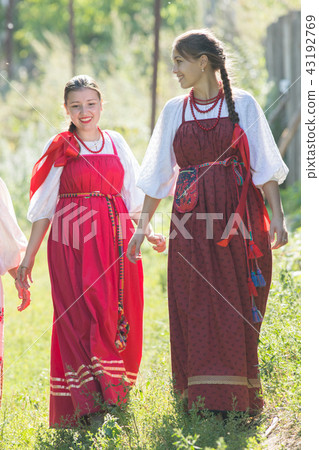 Two young beautiful girls in Russian national dresses are walking on the grass and smiling 43192769