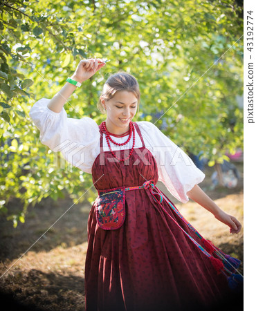 Beautiful young girl in Russian folk sundress dancing on the background of green trees Beautiful young girl in Russian folk sundress dancing on the background of green trees 43192774