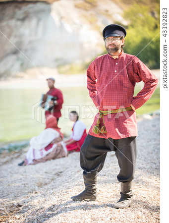 A man in a Russian-folk costume stands on a background of water and poses for the camera A man in a Russian-folk costume stands on a background of water and poses for the camera 43192823