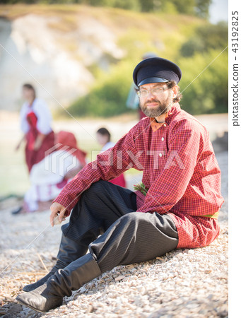 A man in a Russian folk costume sitting on a background of beautiful scenery and friends 43192825