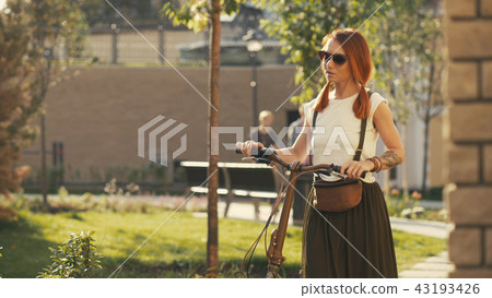 Woman walking beside riding bicycle on city park. Woman bike park Woman walking beside riding bicycle on city park. Woman bike park 43193426
