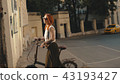 Woman cyclist walking beside riding bike on city road. Woman bike city 43193427