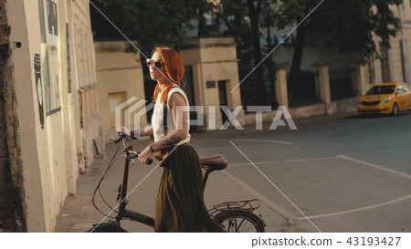 Woman cyclist walking beside riding bike on city road. Woman bike city Woman cyclist walking beside riding bike on city road. Woman bike city 43193427