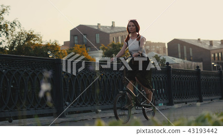 Red haired woman riding bicycle in city on background facade building Red haired woman riding bicycle in city on background facade building 43193442