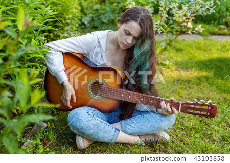 Young woman sitting in grass and playing guitar 43193858