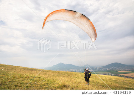 A man paraglider taking off from the edge of the mountain with fields in the background. Paragliding A man paraglider taking off from the edge of the mountain with fields in the background. Paragliding 43194359