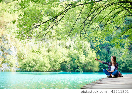 Young happy tourist woman with backpack sitting on wooden bridge enjoying beautiful view 43211891