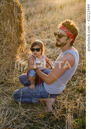 father and son in t-shirts sitting next to a haystack 43212444