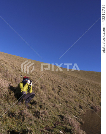 一位穿著登山服裝的男性站在山坡上拍照 43212785