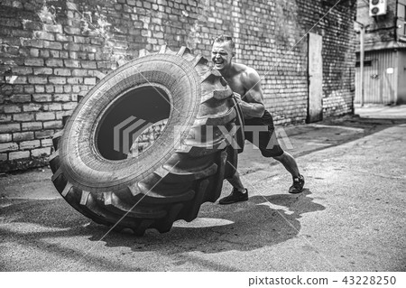 Muscular fitness shirtless man moving large tire. 43228250