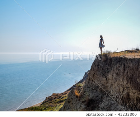 The girl is standing on a cliff near the sea The girl is standing on a cliff near the sea 43232800