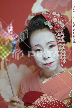 Young Maiko in orange kimono with colorful wind turbine toy in hand. Young Maiko in orange kimono with colorful wind turbine toy in hand. 43237478