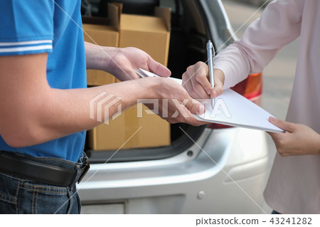 woman signing signature on clipboard to receive package from delivery man. male postal courier person deliver box 43241282