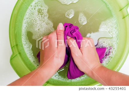 Photo on top of woman hands washing violet clothes in green basin with foam water Photo on top of woman hands washing violet clothes in green basin with foam water 43255401