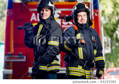 Photo of two young firemen with axes in hands near fire engine 43255565