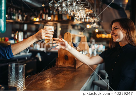 Male barman passes glass of beer to female visitor 43259247