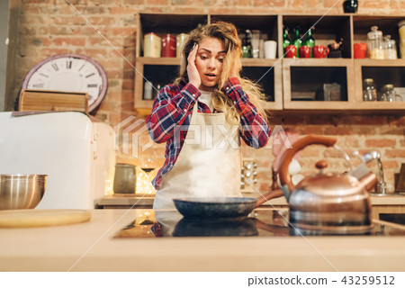 Amazed housewife in an apron looking on frying pan 43259512