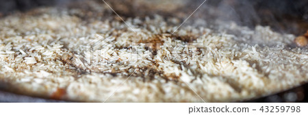 cooking Rice for pilaw or paella in iron cauldron over open fire. Smoke and steam. Tasty food 43259798