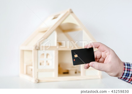 Hand holding black plastic chip card. Wooden house model on background. Wire payment transfer 43259830