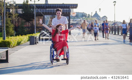 Guy rolls a happy disabled girl in a wheelchair on the waterfront 43261641