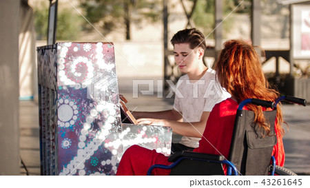 Young man plays the piano for a red girl in a wheelchair 43261645