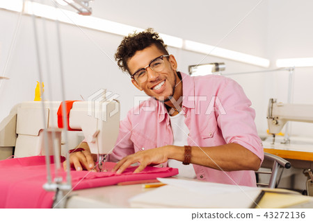 Cheerful young tailor smiling happily and enjoying his working day Cheerful young tailor smiling happily and enjoying his working day 43272136