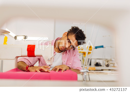 Serious young man leaning his head while using the sewing machine Serious young man leaning his head while using the sewing machine 43272137