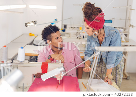 Serious tailor looking at his experienced colleague and listening to her Serious tailor looking at his experienced colleague and listening to her 43272138