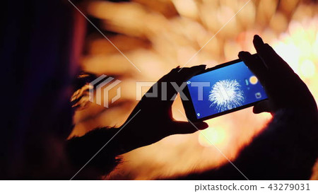 A woman shoots fireworks on a smartphone. The lights are beautifully reflected in her glasses 43279031