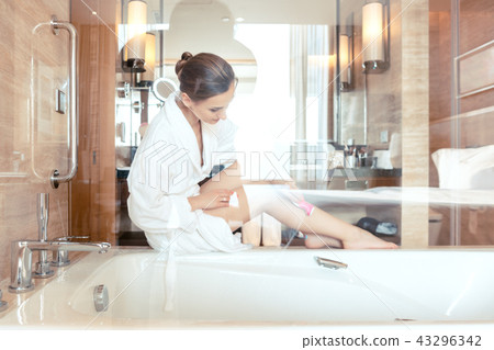 Woman removing hair by shaving her legs in bathroom of hotel Woman removing hair by shaving her legs in bathroom of hotel 43296342
