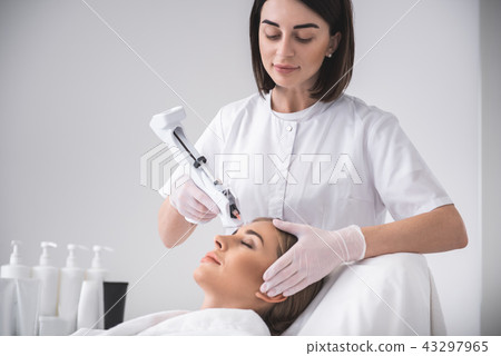 Young beautician making injection in girl forehead while lady laying at daybed 43297965
