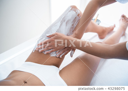Beautician hands applying cosmetic white clay on lady leg 43298075