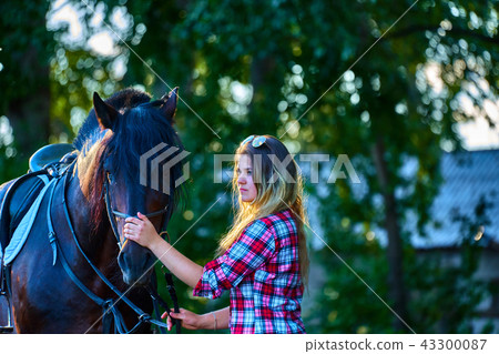 Beautiful girl with long hair on a walk with a horse. Summer evening. 43300087