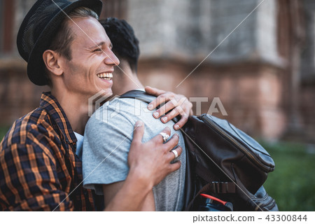 Pleased male hugging comrade during walk outdoor Pleased male hugging comrade during walk outdoor 43300844
